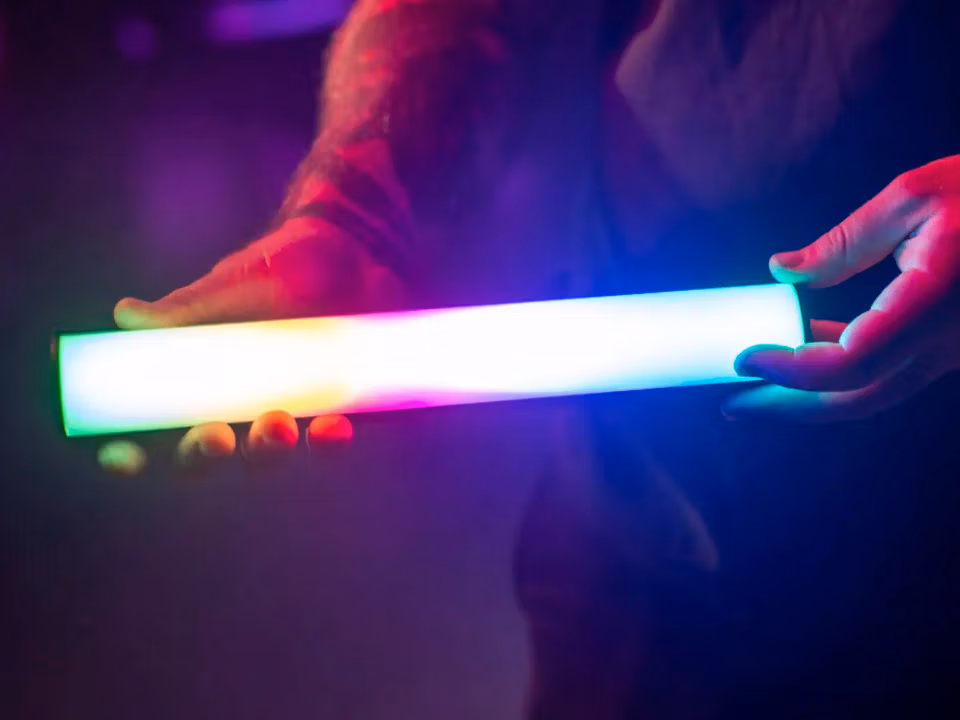 Cвітлодіодна трубка Aputure MT Pro RGBWW Mini LED Tube (APA0202A10) 7 Рука тримає ввімкнений світлодіодний тьюб Aputure MT Pro з переливом кольорів на знімальному майданчику